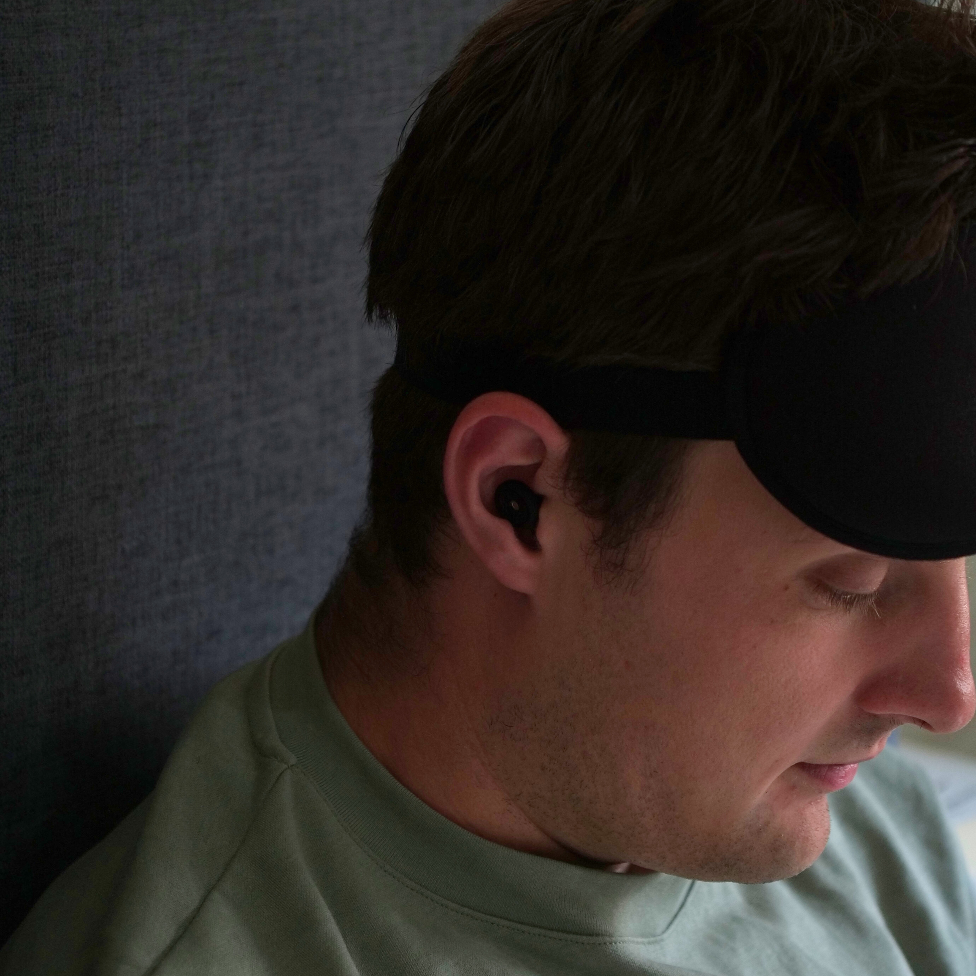 Man wearing a black sleep mask and silicone earplugs. 