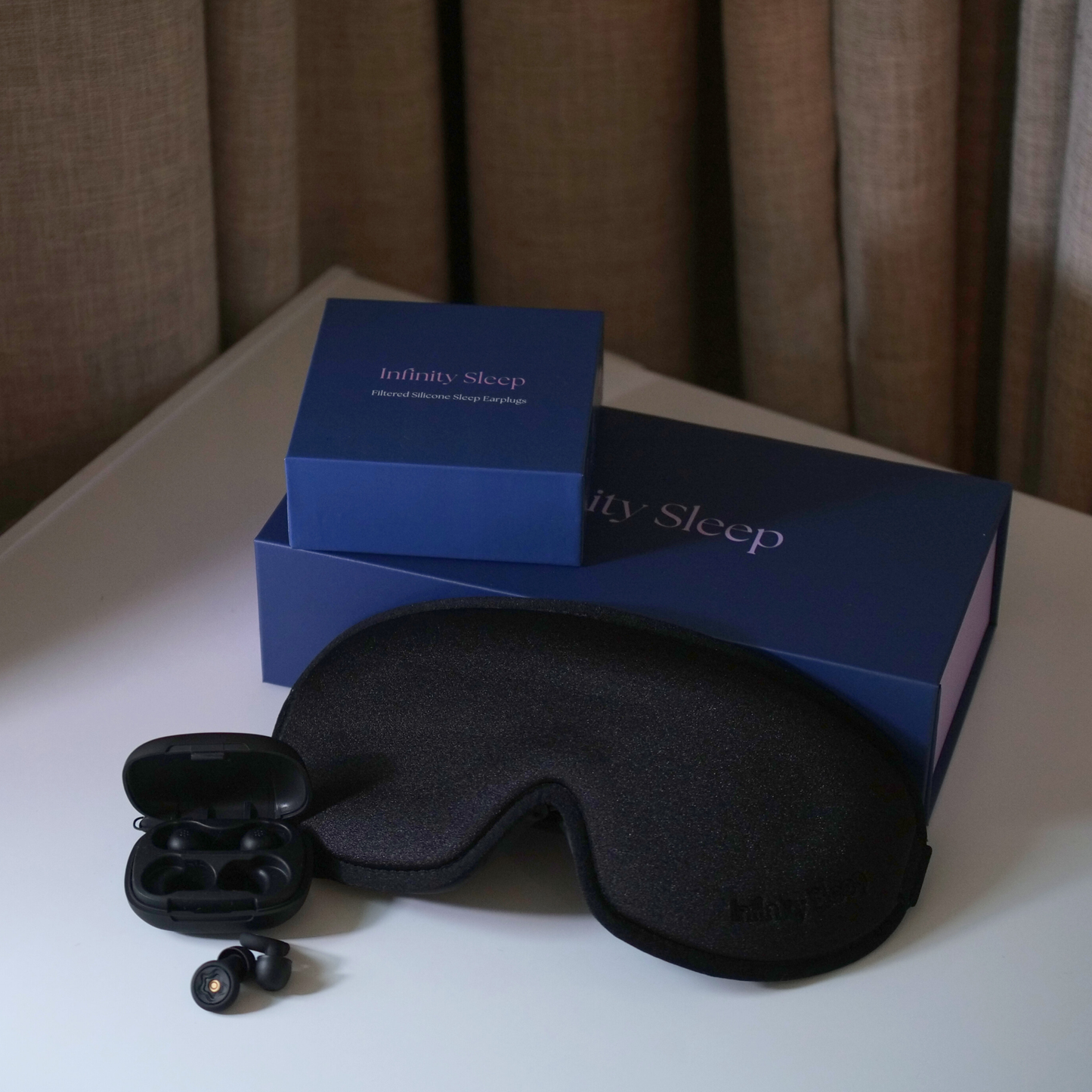 Black sleep mask and earplugs with 'Infinity Sleep' packaging on a white surface.